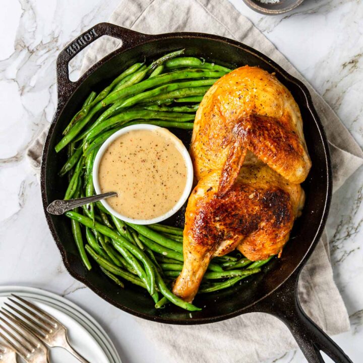 roasted half chicken with crispy golden skin in a skillet with green beans and gravy