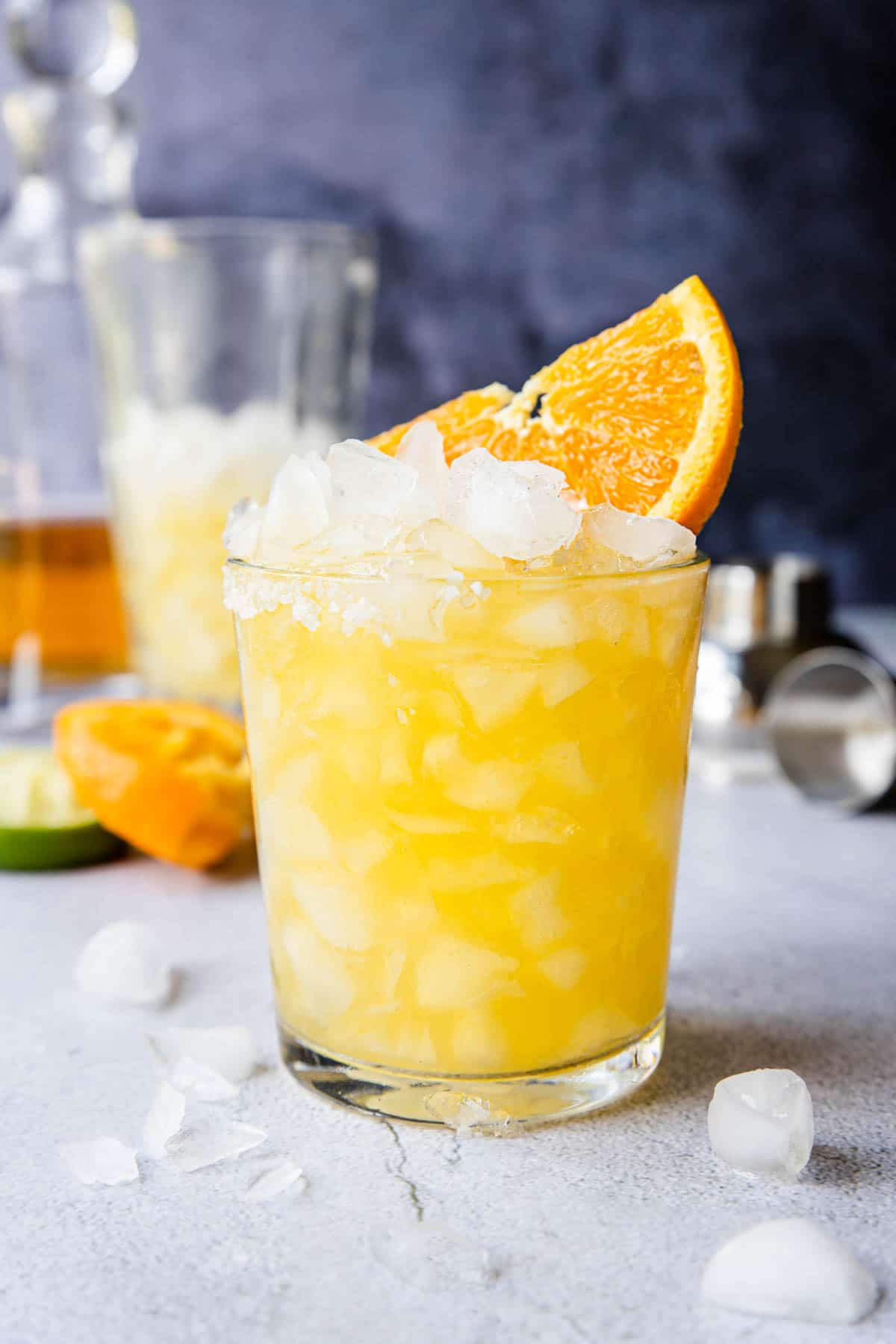 orange margarita in a glass with a little salt on the rim, ice piled high and a large orange wedge in the top