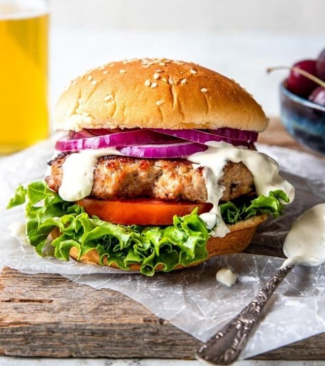 Grilled Pork Burger on a bun with lettuce, tomato, onion and garlic cream sauce