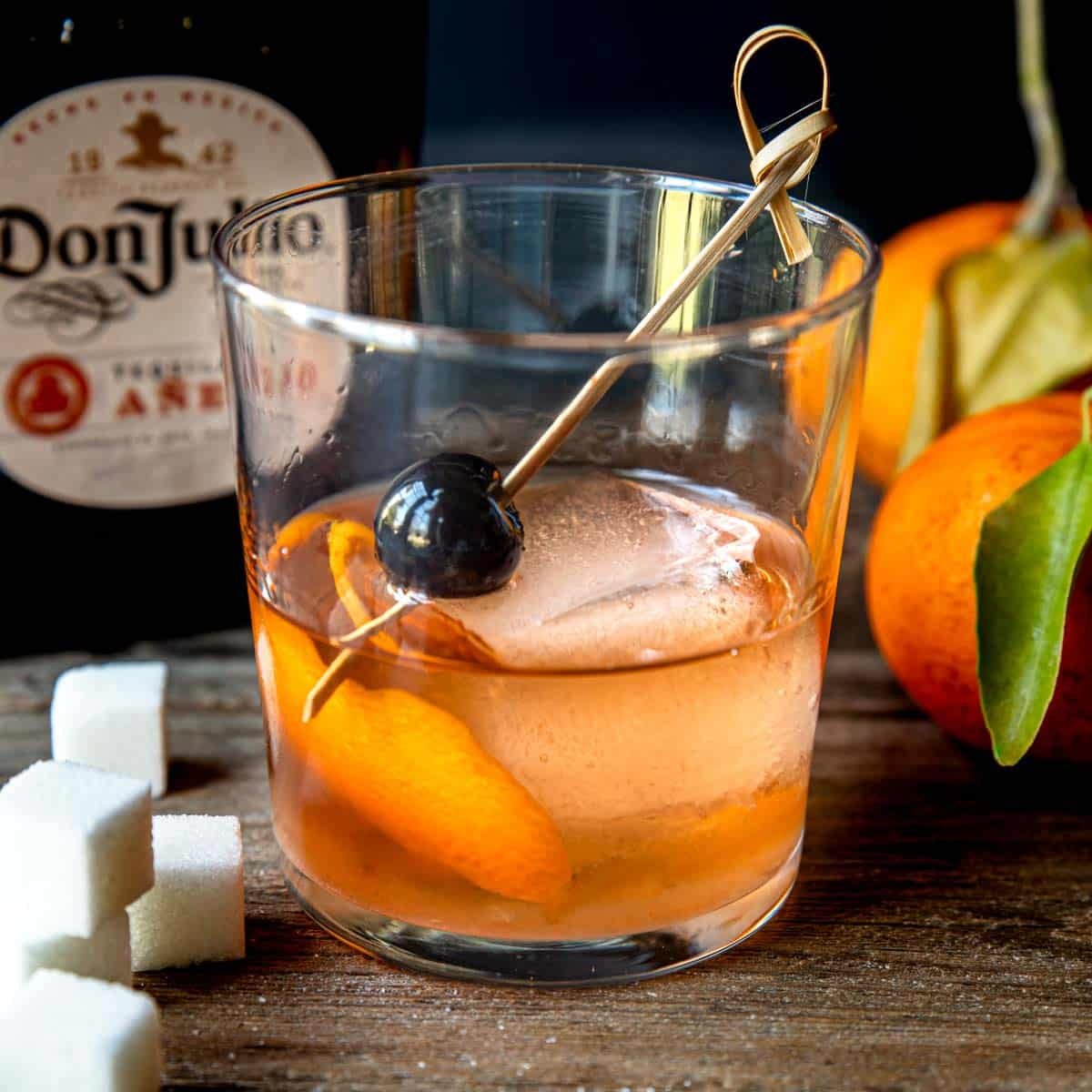 Anejo old fashioned with a large ice cube and an orange peel and Luxardo cherry