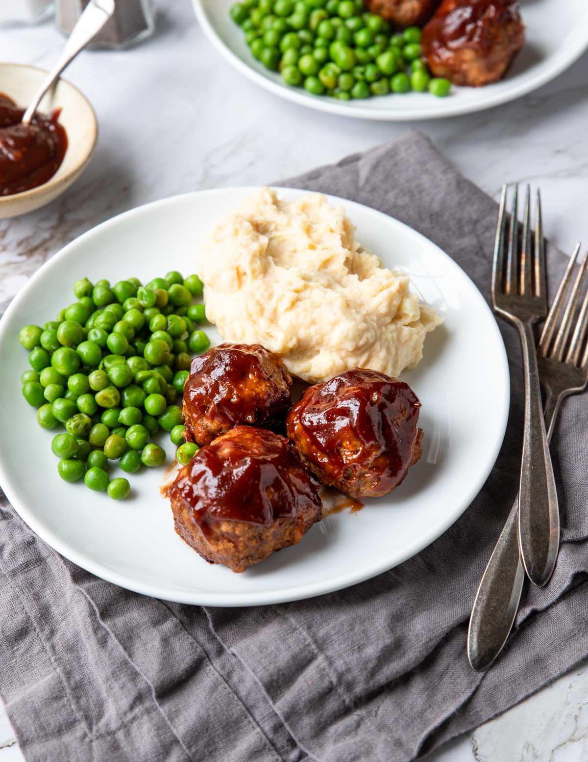 a dinner plate with bbq meatballs peas and mashed potatoes