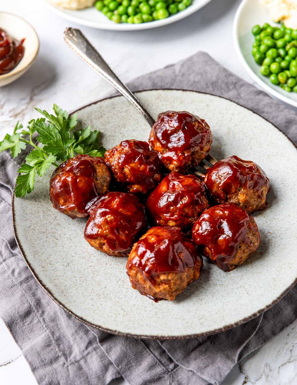 bbq meatballs on a plate with peas and mashed potatoes in the back
