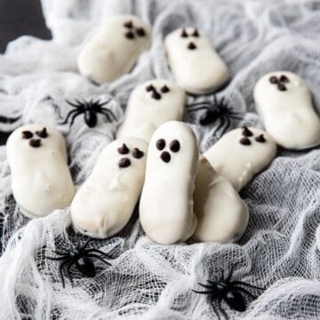 a couple ghost cookies on a spider web with spiders