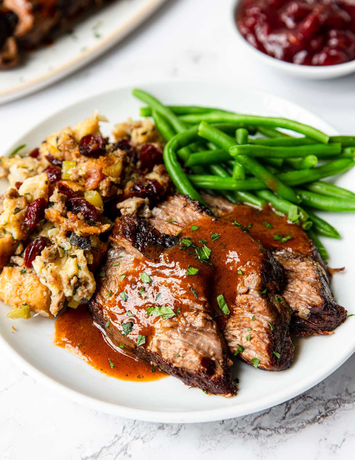 a plate of sliced tri tip with stuffing and green beans