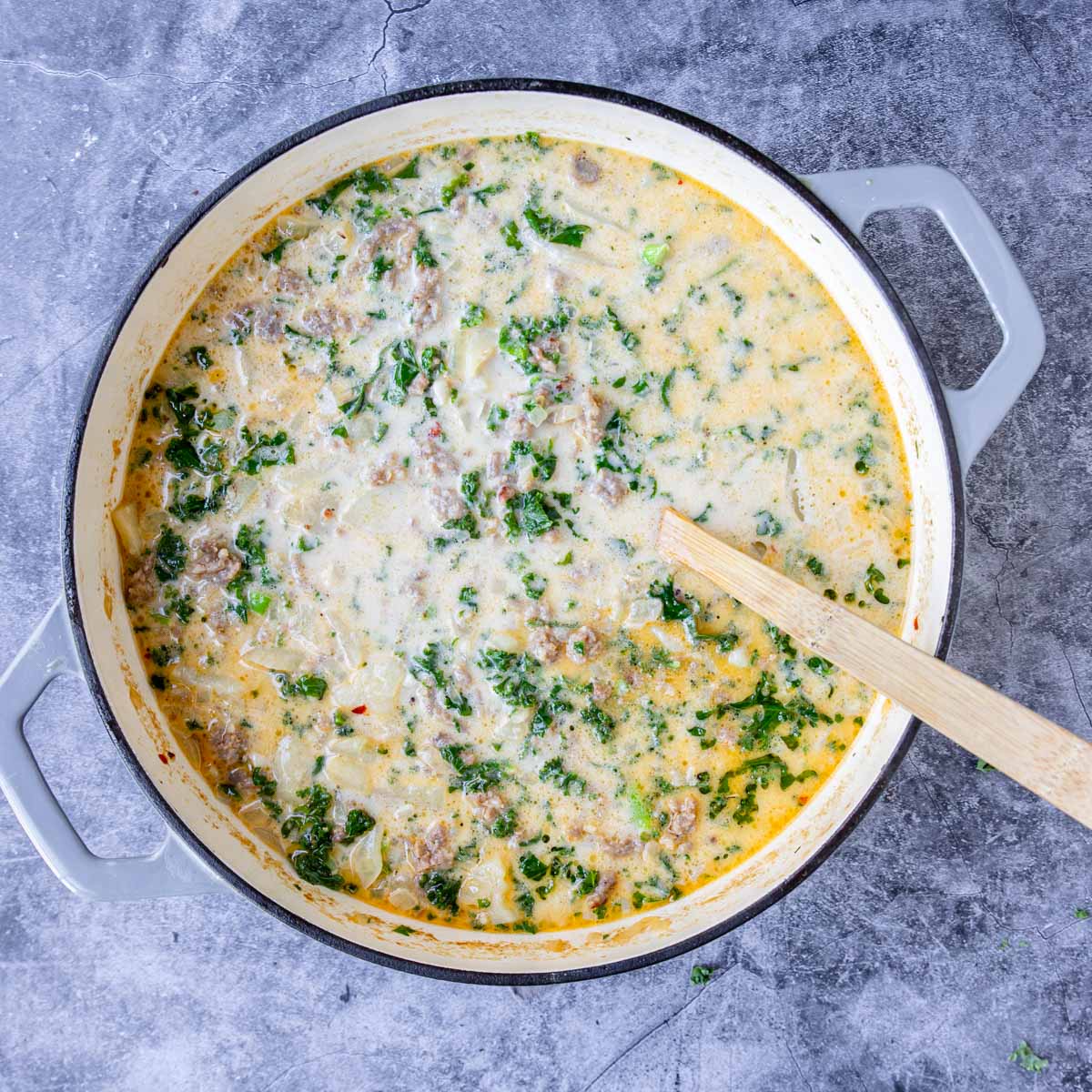 kale and cream added to zuppa toscana in a large pot