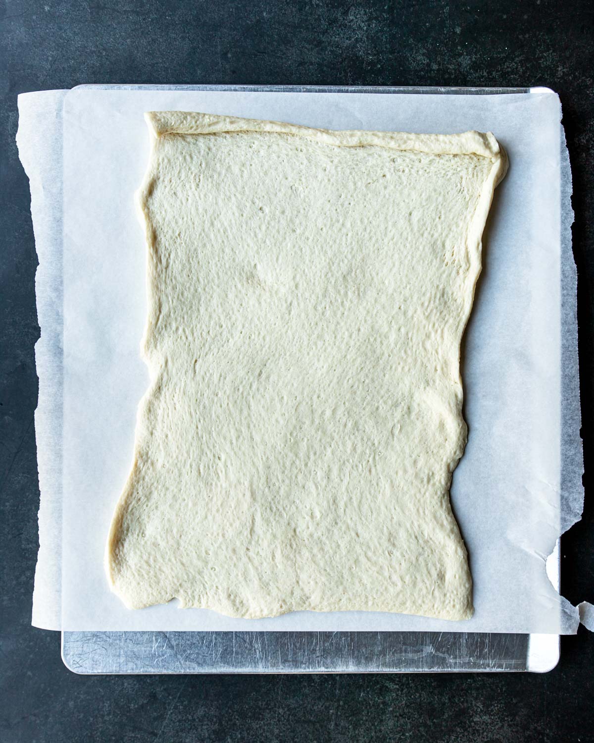 pizza crust unrolled on a parchment paper lined baking sheet