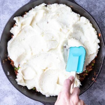 Spatula spreading mashed potatoes on Shepherd's Pie