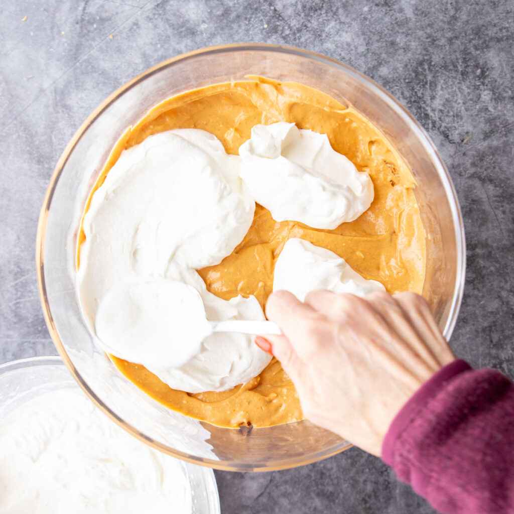 spreading whipped cream in a trifle bowl over top pumpkin filling