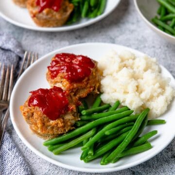 a plate with two turkey meatloaf muffins, green beans and mashed potatoes