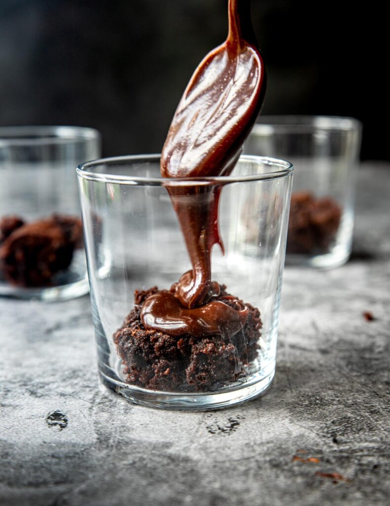 fudge being drizzled on brownies in a cup