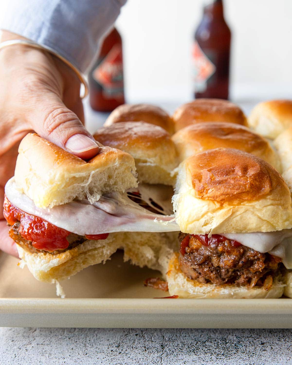 pulling a meatloaf slider from the tray and cheese is stringing between sandwiches