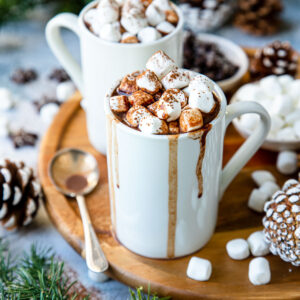 a white mug with hot chocolate dripping down the sides and filled with hot cocoa topped with marshmallows