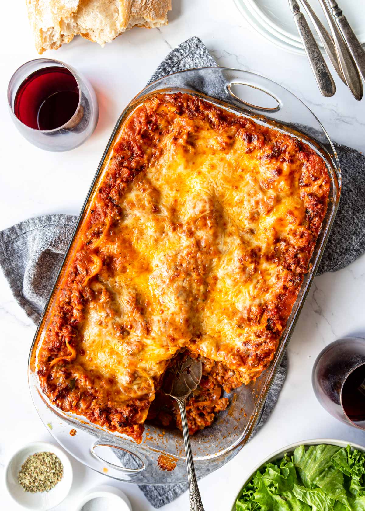 a table with a baked lasagna in the middle and wine, bread and salad around