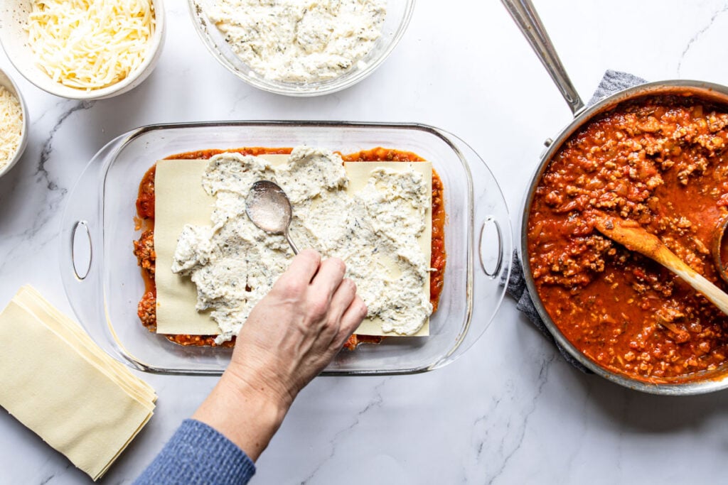 spreading ricotta on top of lasagna noodles