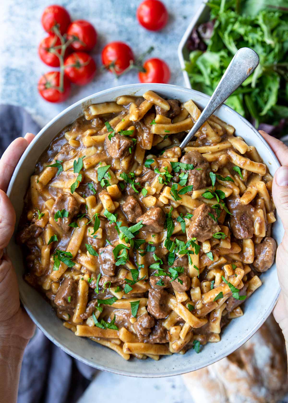 a bowl of beef and noodles being held above a table