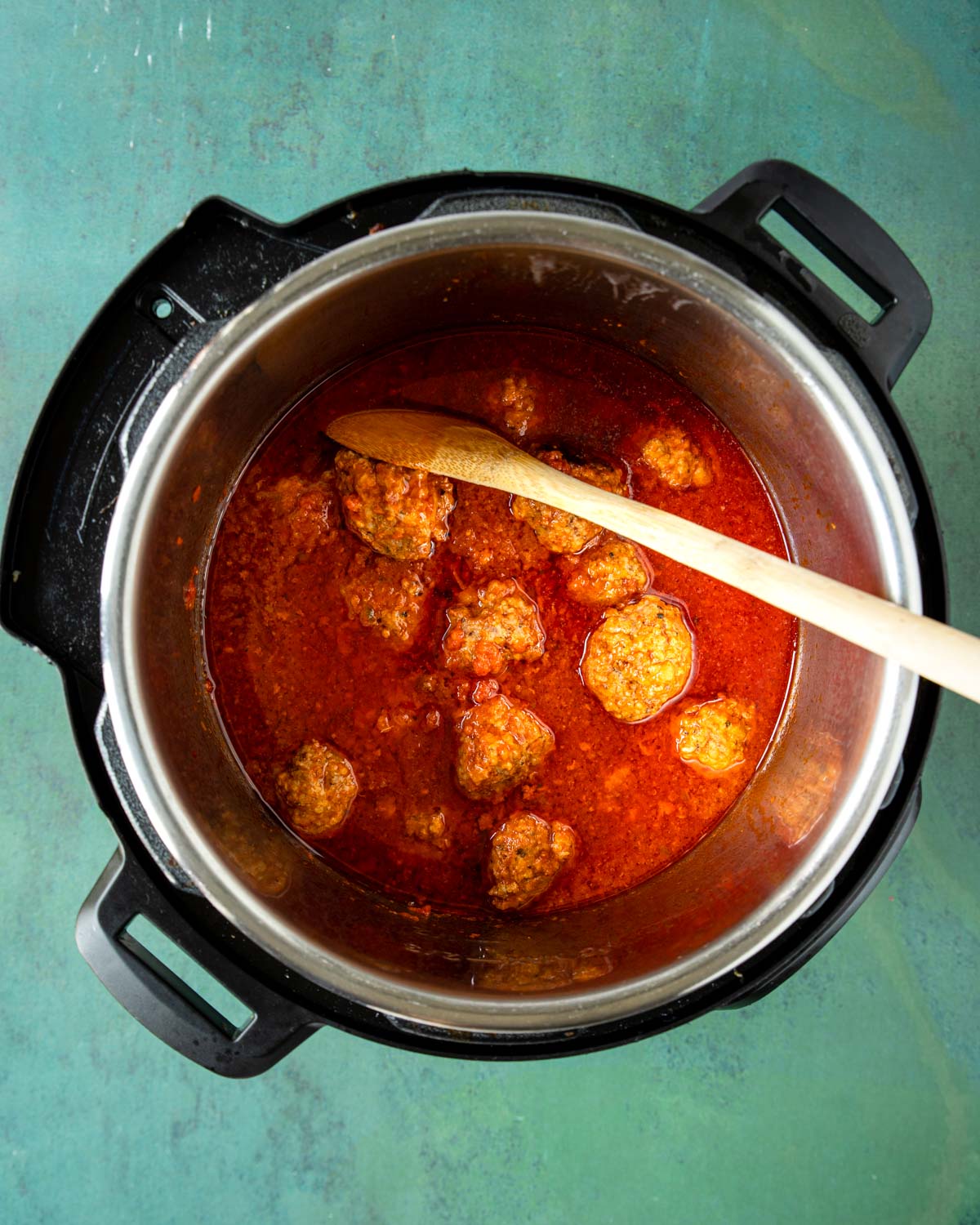 meatballs cooked in the Instant Pot with a wooden spoon stirring