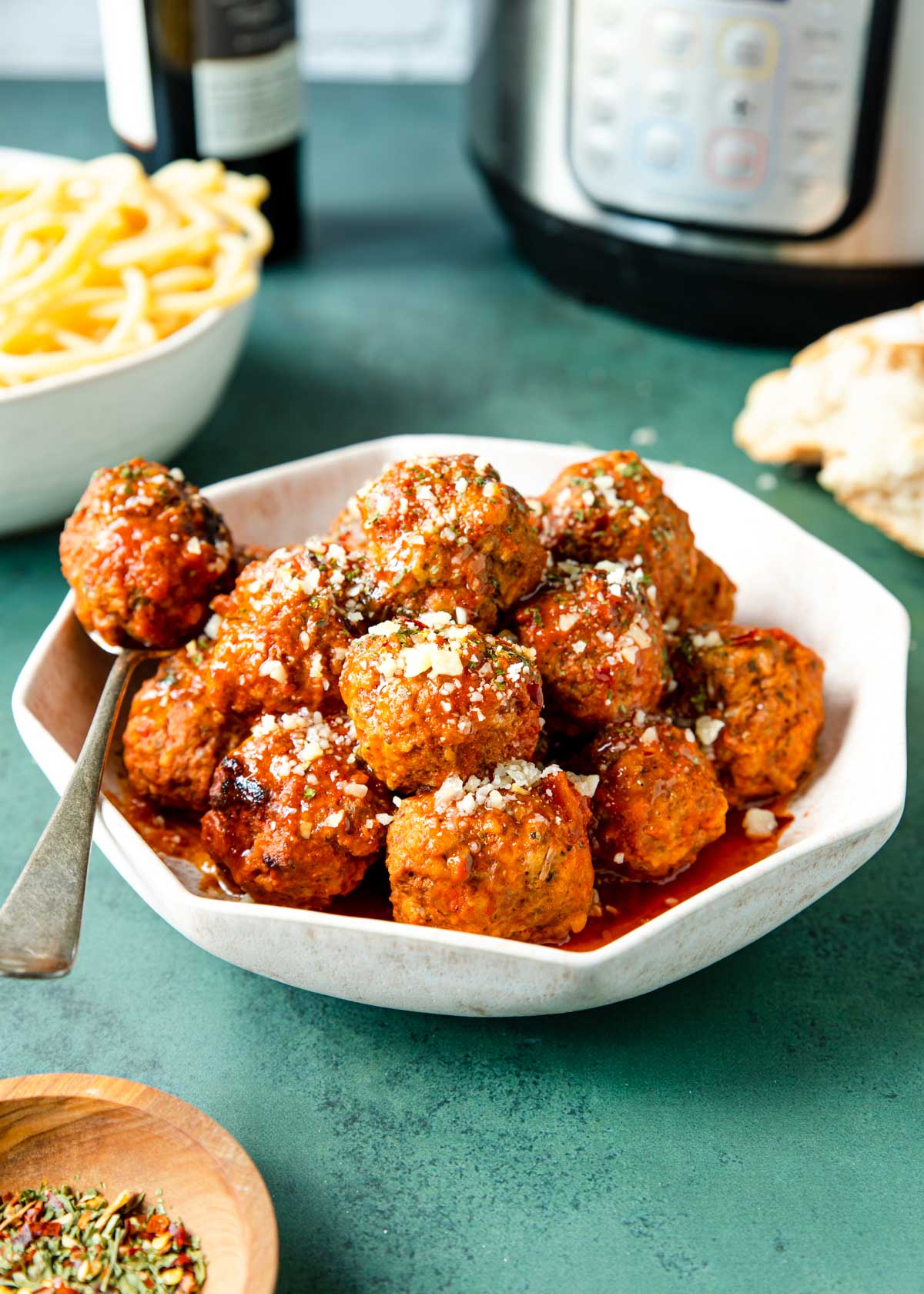 Meatballs in a bowl with parmesan sprinkled on top, Instant Pot and spaghetti in the back