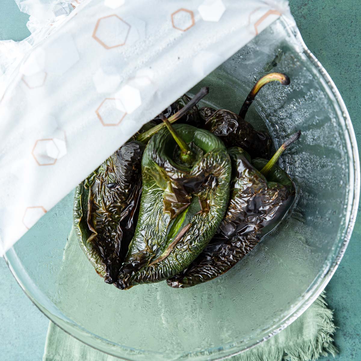 roasted poblano peppers in a bowl covered with plastic wrap