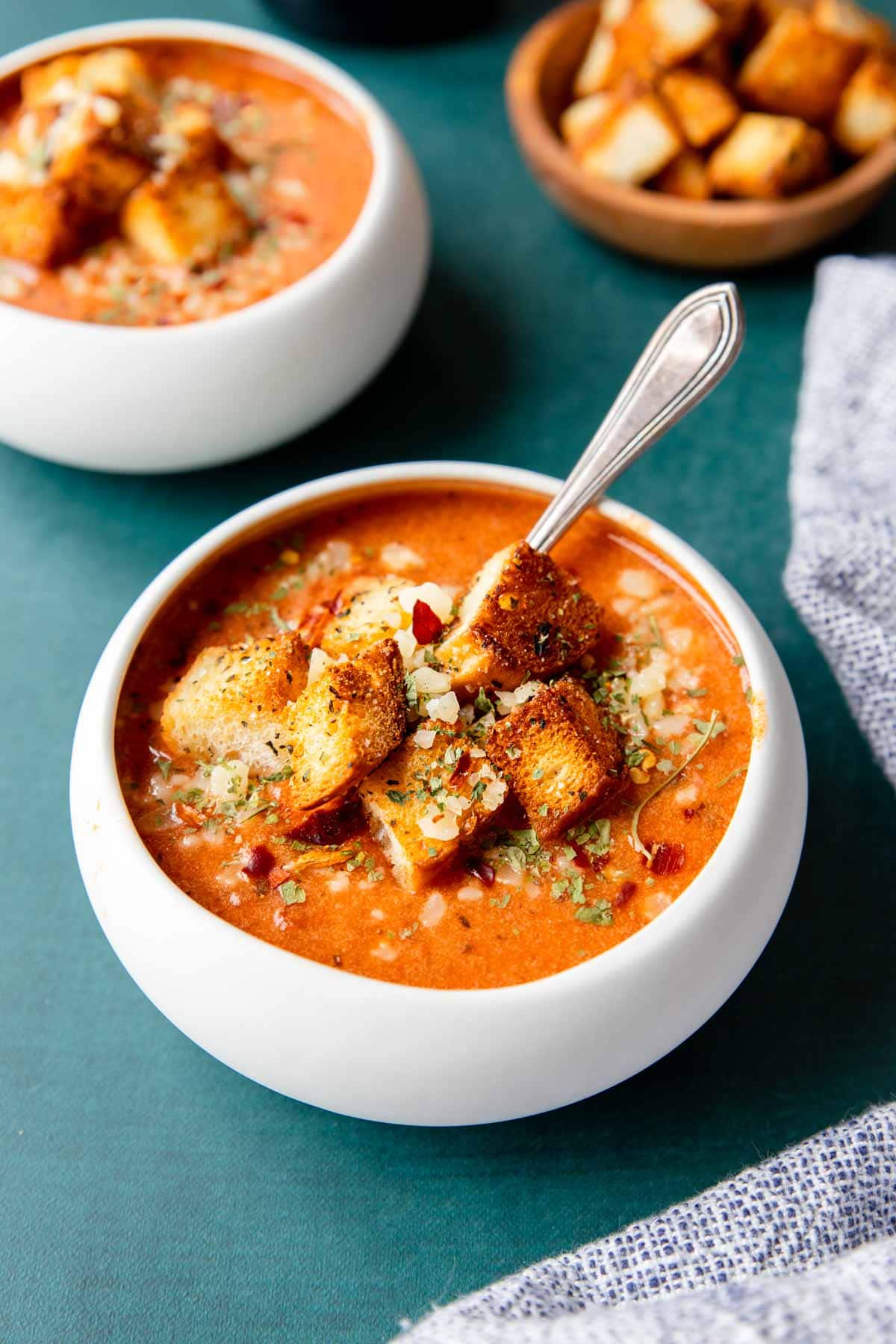 two bowls of tomato basil soup with croutons on the top