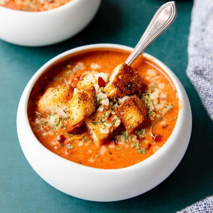 tomato basil soup in a white bowl with croutons and parmesan on top
