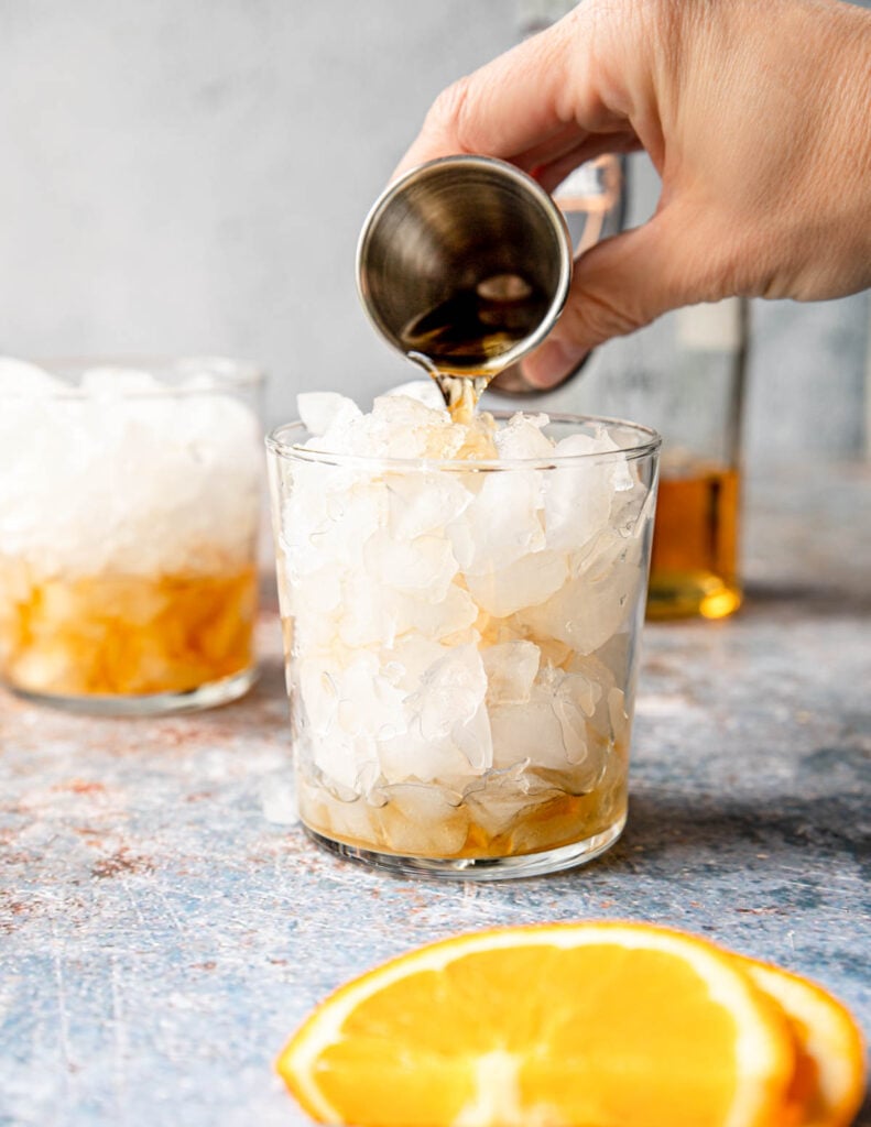 pouring Añejo tequila into an ice filled glass 