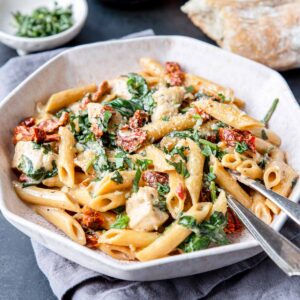a bowl of creamy penne pasta with sun dried tomatoes, chicken and spinach