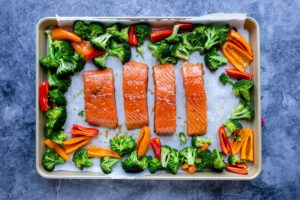 showing how to place the veggies and marinated salmon on the baking sheet