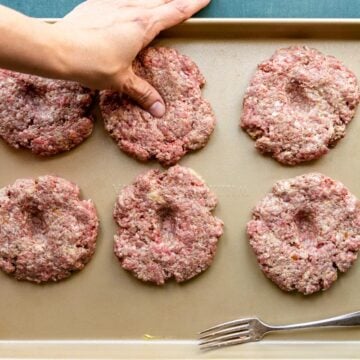 6 burger patties with a thumb pressing a dent in the middle of one patty