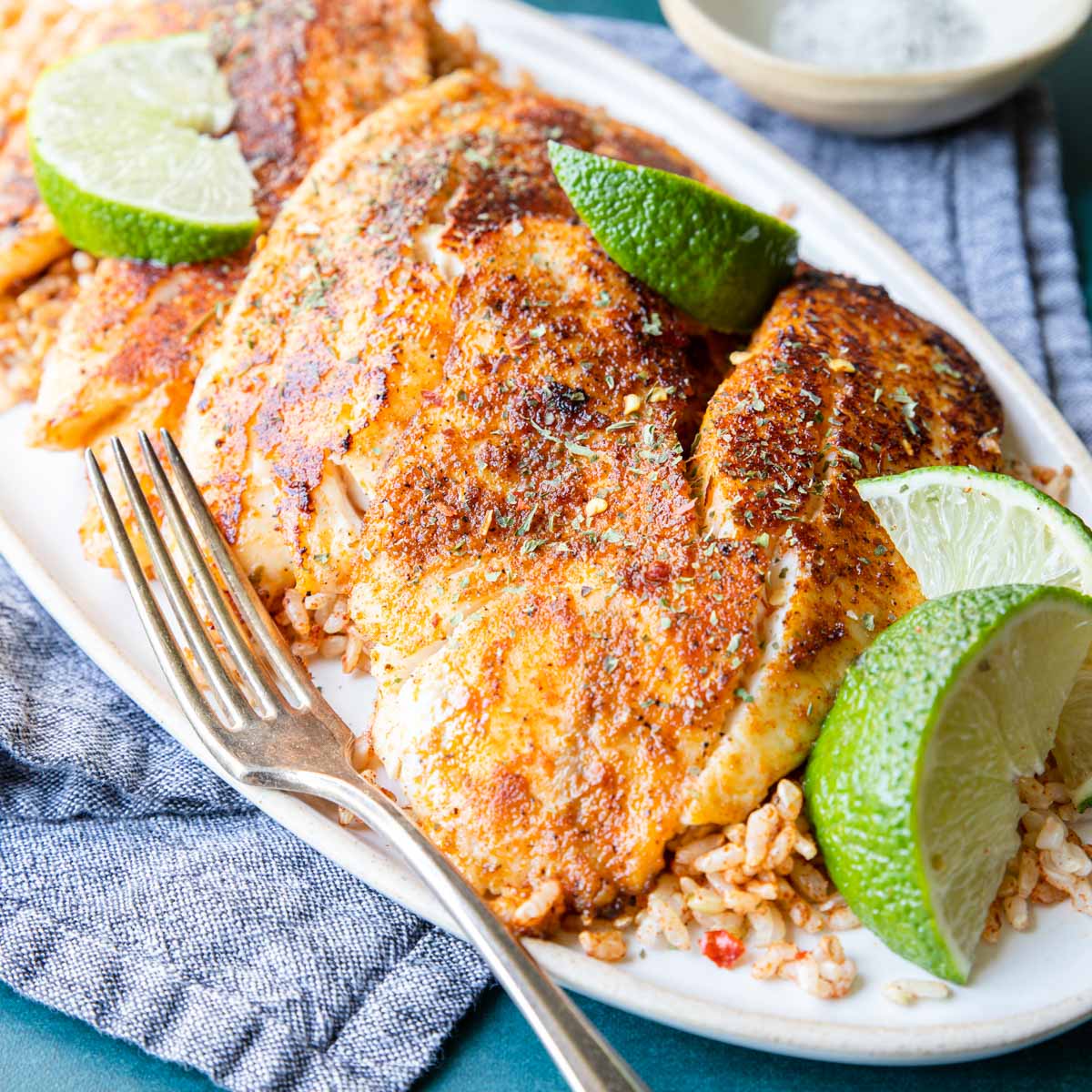 blackened tilapia filets with lime wedges and dirty rice
