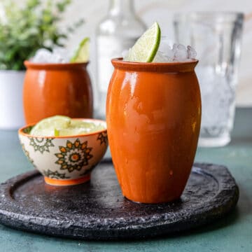 cantarito drink in a clay cup garnished with a lime wedge