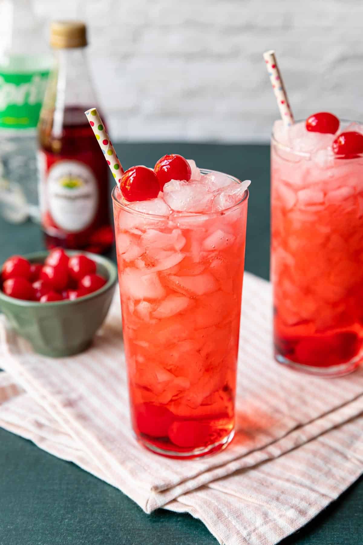 two tall glasses with red Shirley Temple Drinks, garnished with maraschino cherries