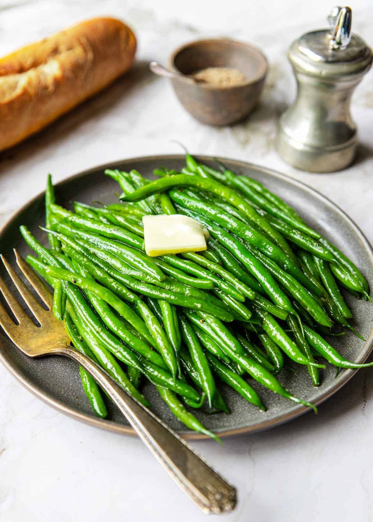 haricot verts on a plate with a pat of butter and a baguette in the back