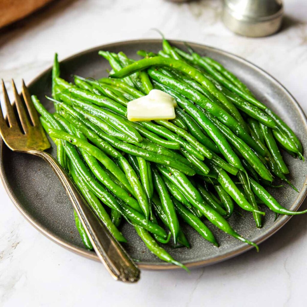 cooked haricot verts on a plate with a pat of butter