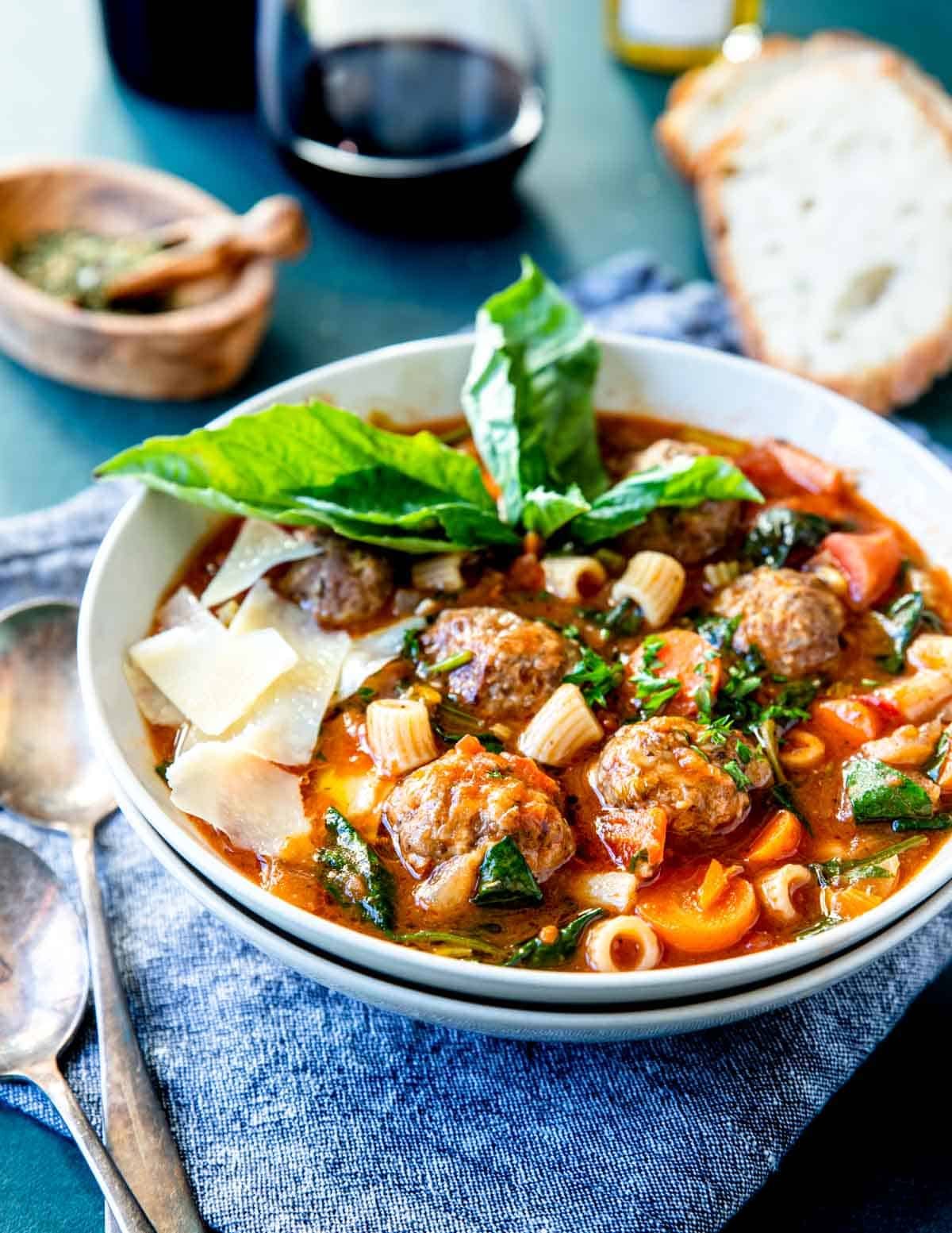 a big bowl of meatball soup with parmesan and basil over top