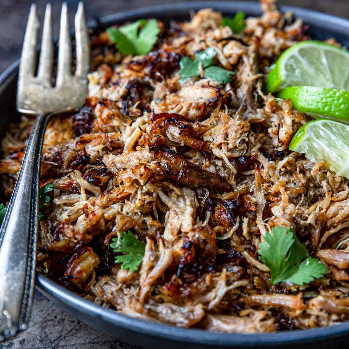 Instant Pot Carnitas in a bowl with lime wedges and a fork