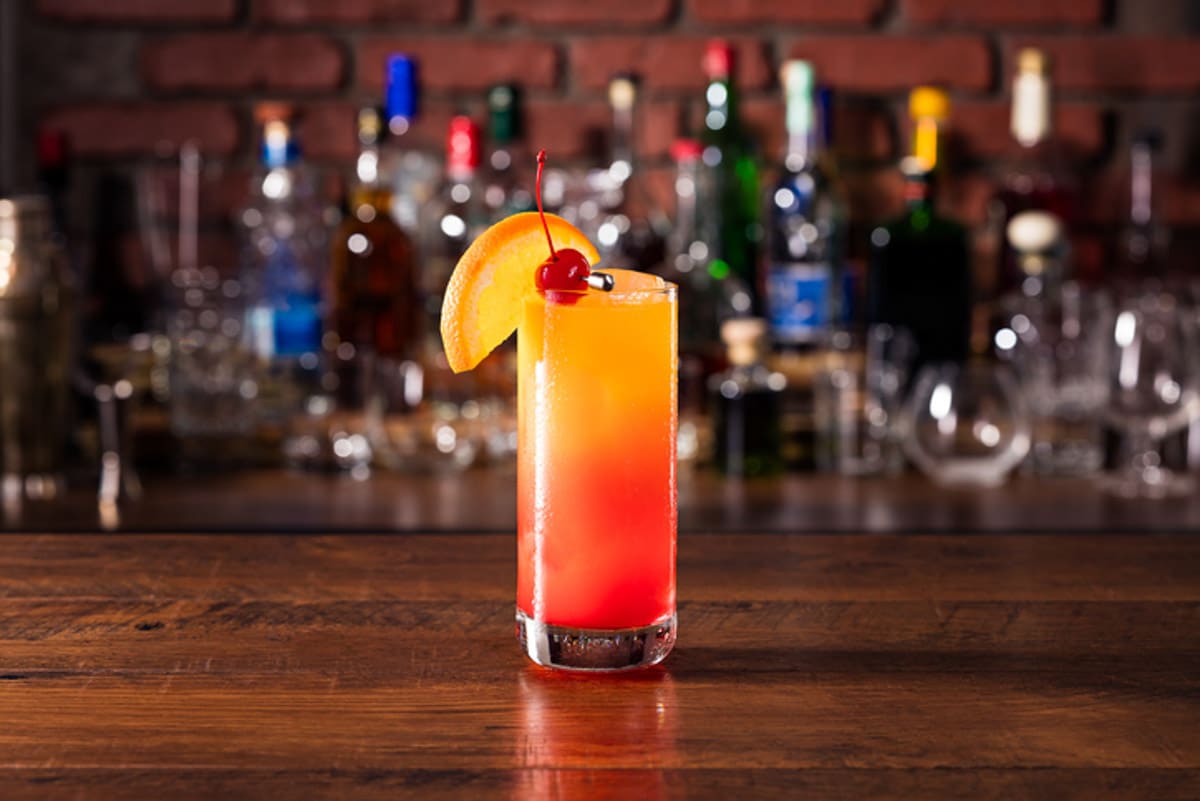 a tequila sunrise cocktail with a cherry and orange on a bar