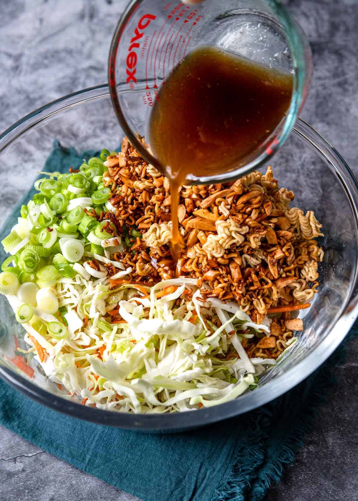pouring dressing over a slaw mix with ramen noodles and almonds