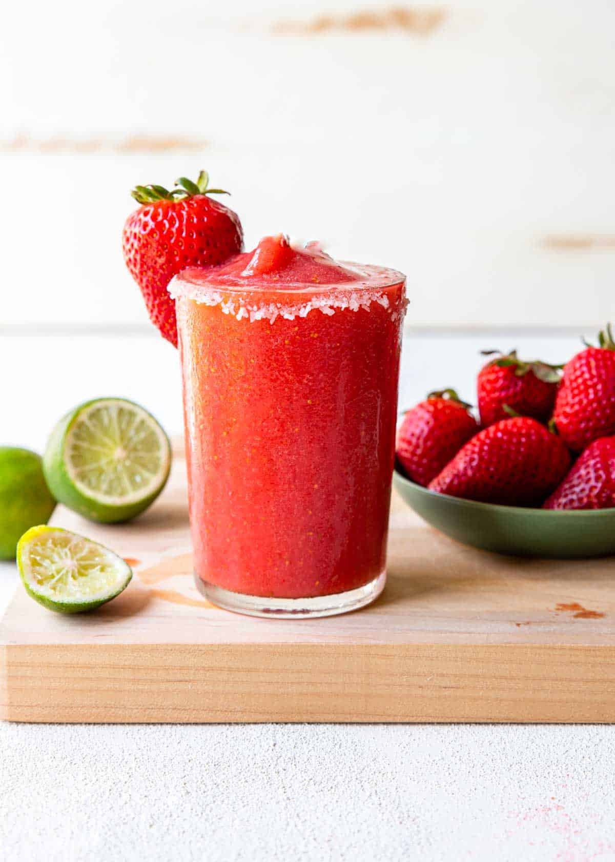 Frozen Strawberry margarita on a table with strawberries and limes