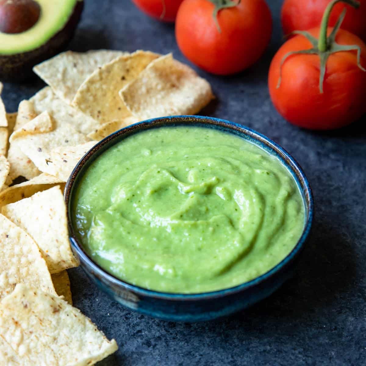 green salsa with avocado in a bowl with tomatoes and chips to the side