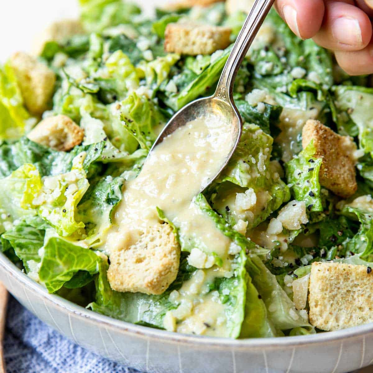 close photo of romaine caesar salad with dressing being spooned on