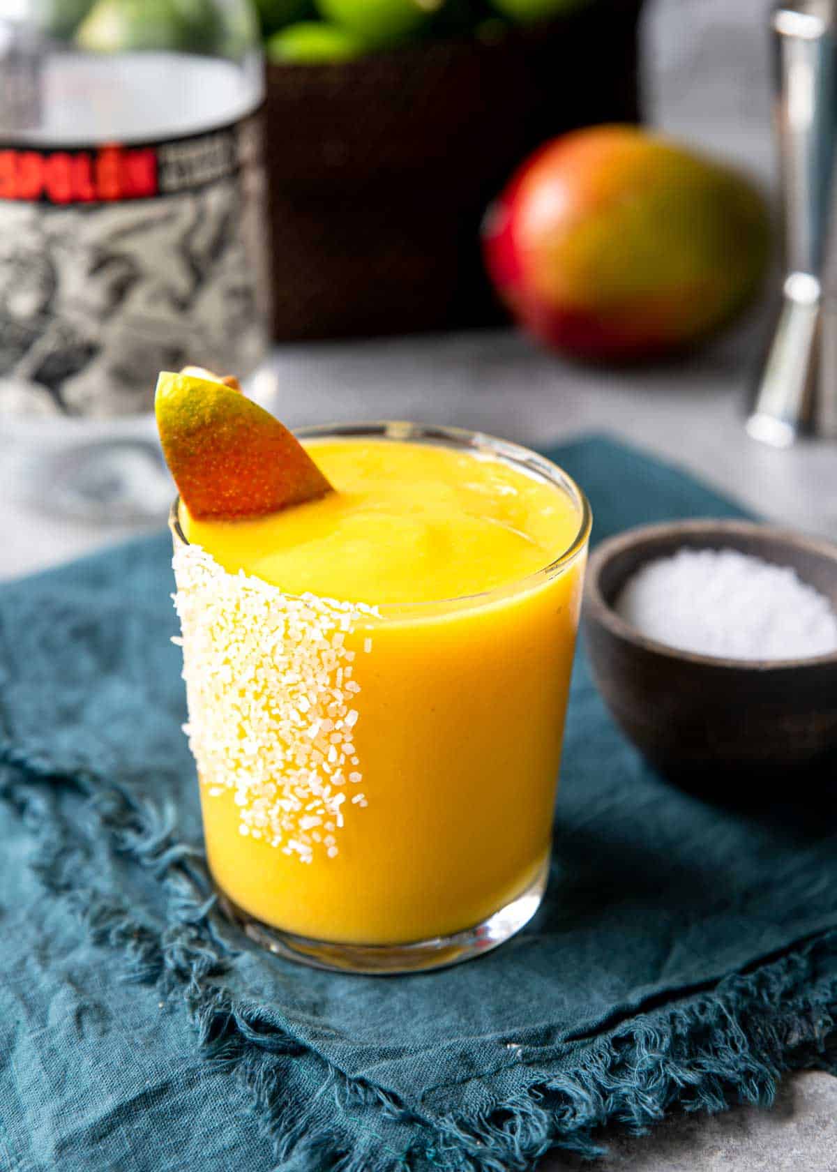 a glass with frozen mango margarita with a fresh piece of mango