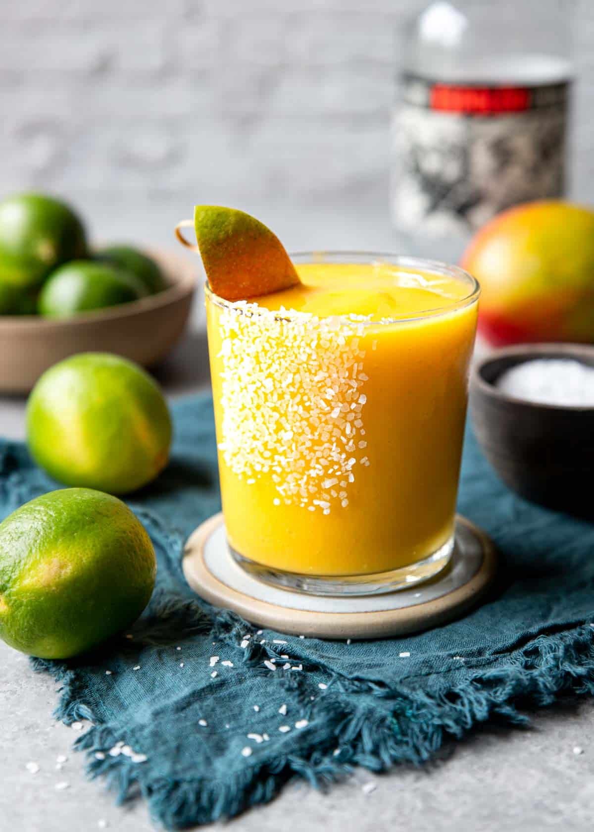 frozen mango margarita in a salt rimmed glass with limes to the side