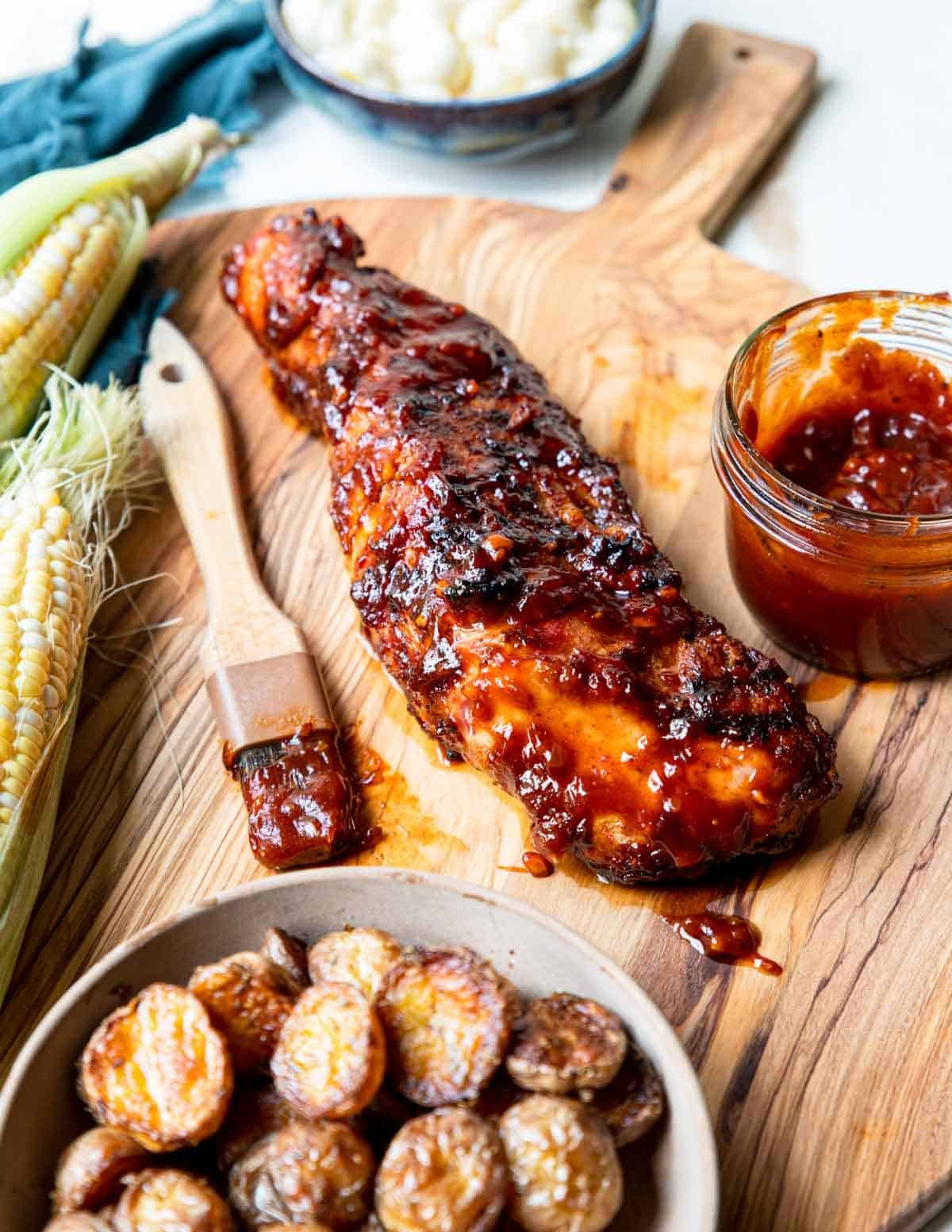 grilled BBQ pork tenderloin on a cutting board with bbq sauce and a brush