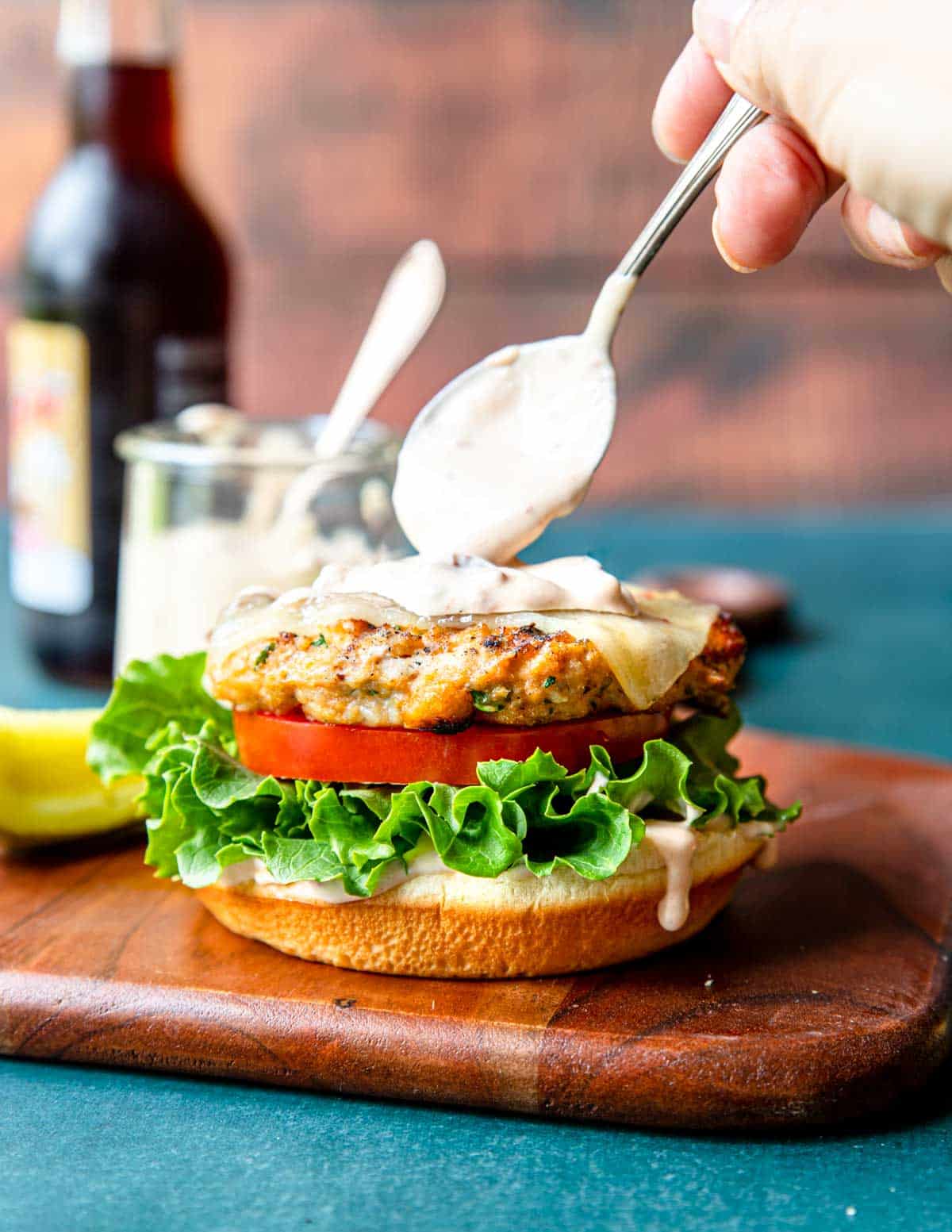 spooning aioli on top of a grilled chicken burger with pepper jack cheese