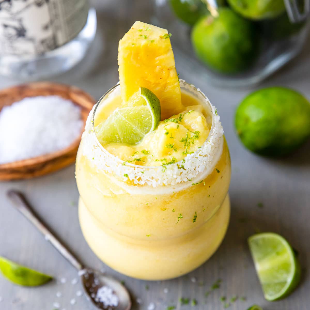 blended pineapple margarita in a glass with fresh pineapple and lime zest on top