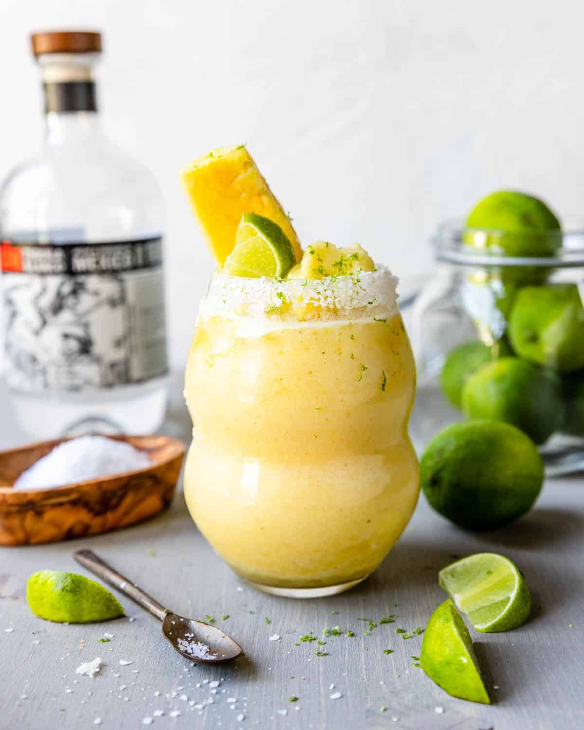 Frozen Pineapple Margarita in a glass, garnished with lime wedge and pineapple slice