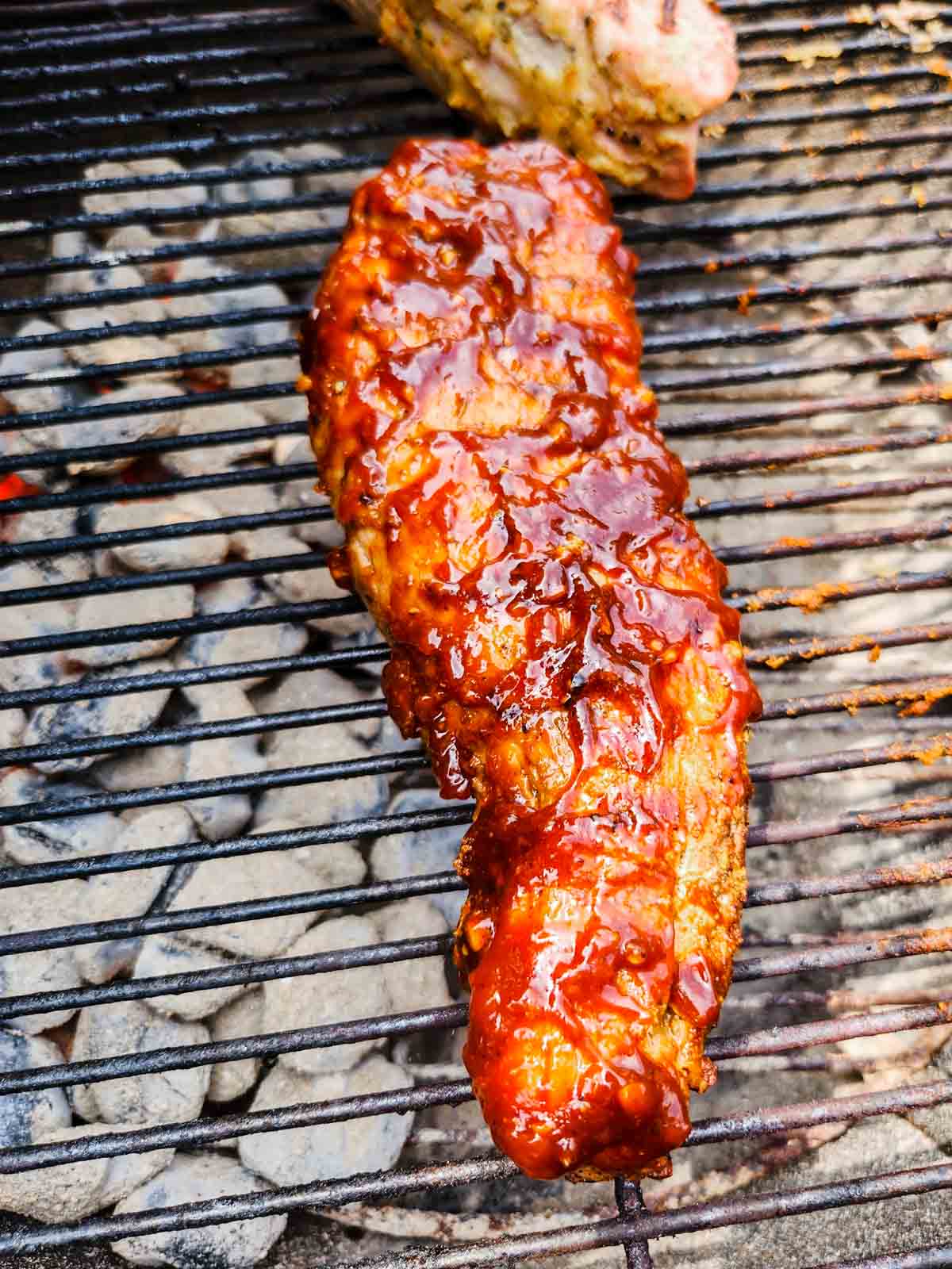bbq pork tenderloin on a grill, basted with bbq sauce