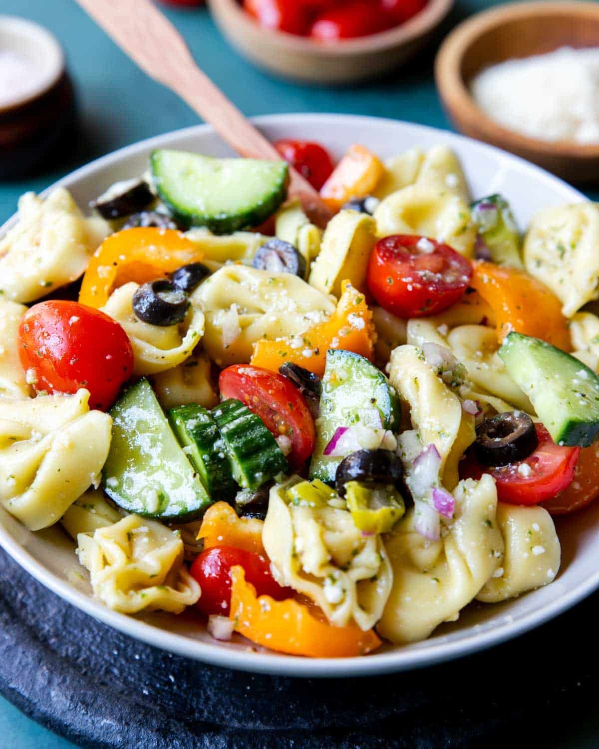 bowl of cheese tortellini with veggies and dressing in a white bowl with a wooden spoon 