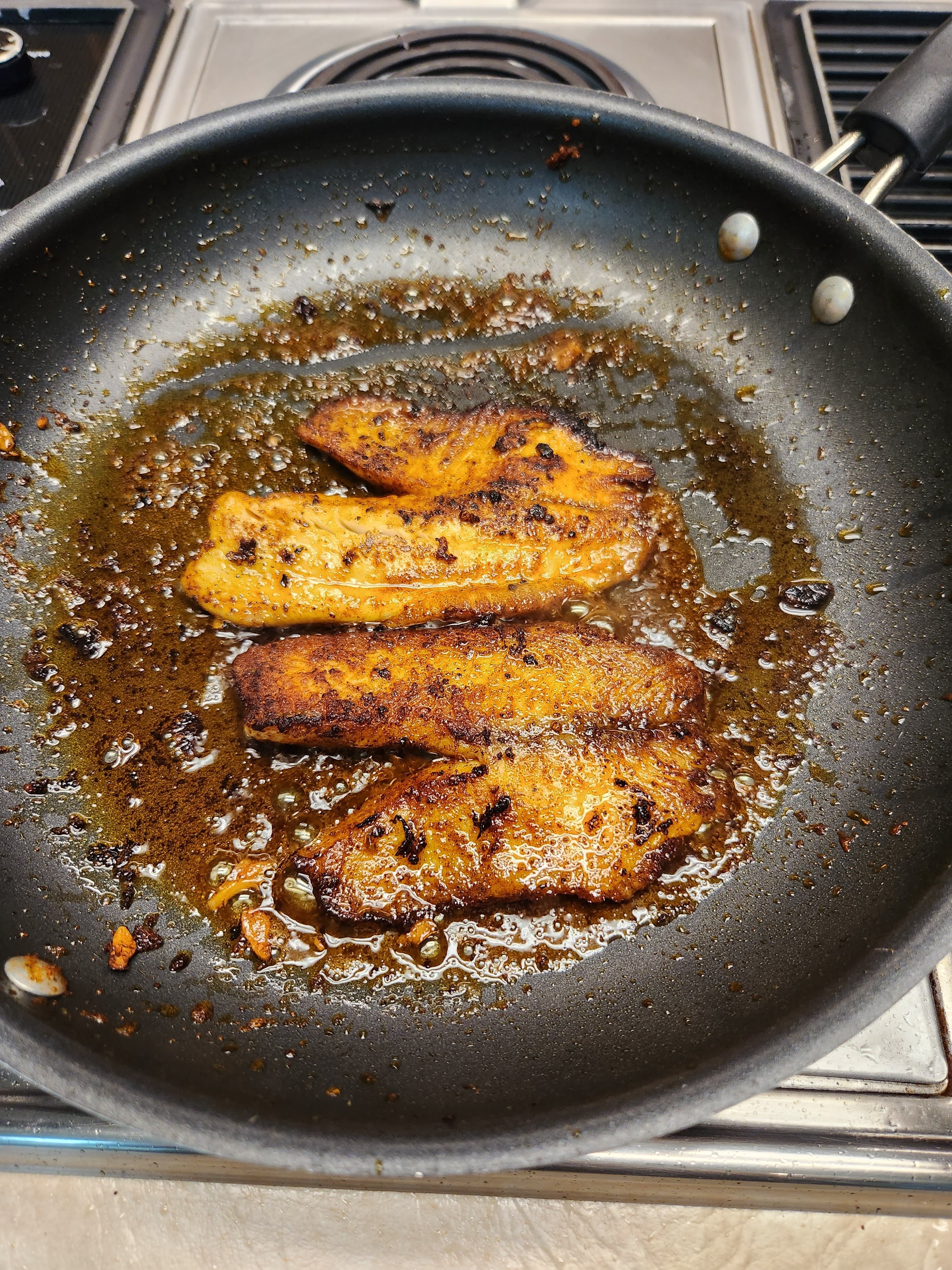 Tilapia filets being fried in a pan