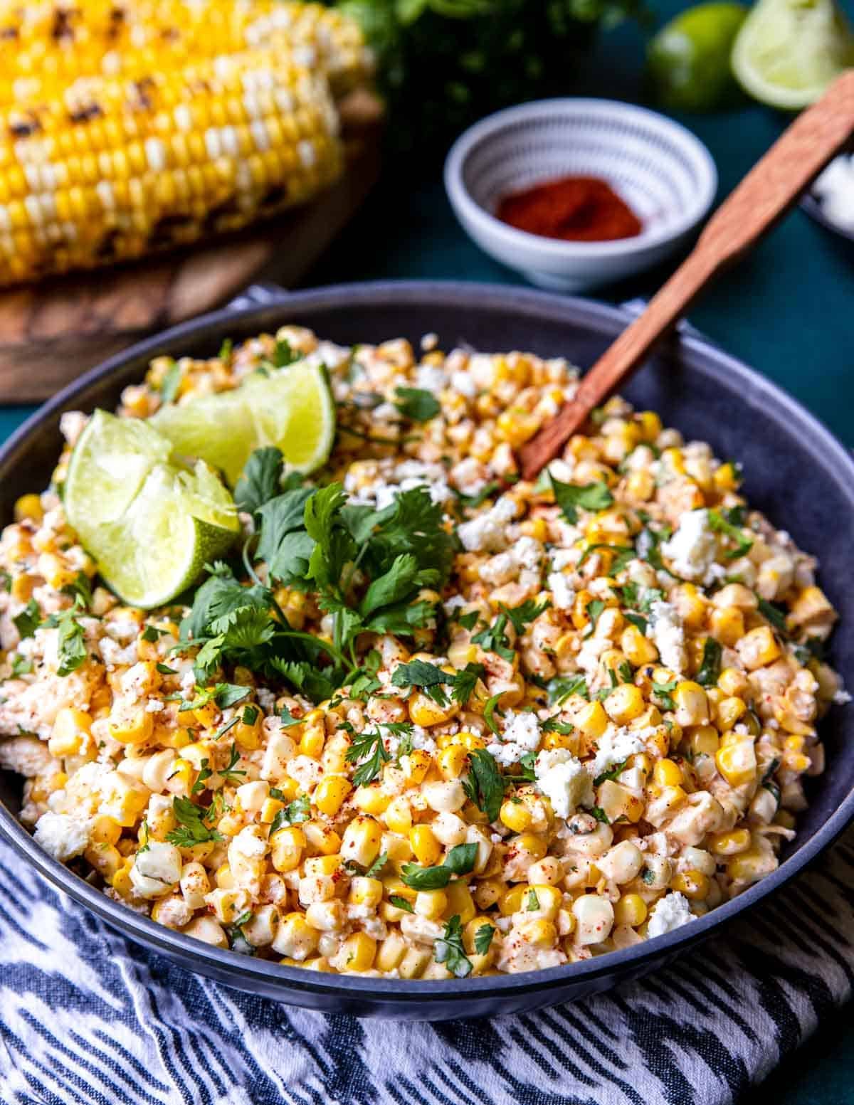 a grey bowl of Mexican Street Corn Salad with cilantro and limes on top